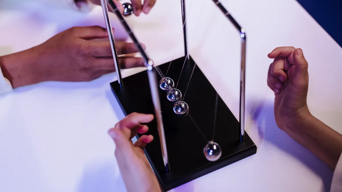 A Newton's cradle, a desk toy consisting of a series of metal balls suspended from a frame, with the balls in motion.