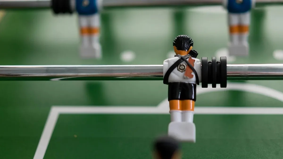 A close-up of a Lego figure standing on a green table with white lines, likely a foosball table.